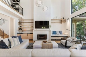 A modern living room with a fireplace, a flat-screen TV, and a staircase.