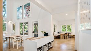 Una cocina moderna con suelo de madera, armarios blancos y una isla central. Varias ventanas ofrecen luz natural y vistas al exterior.