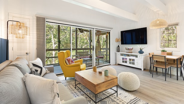 A spacious living area with a sofa, coffee table, and dining table. Large windows provide natural light and a view of the outdoors. - New reno, Boho-style "treehouse" at the beach! (Kiawah Island)