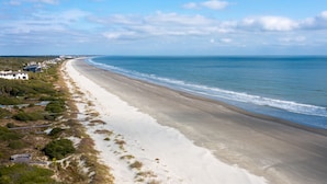A coastal beach with a long stretch of sand, a few buildings along the shore, and a clear view of the ocean. - New reno, Boho-style "treehouse" at the beach! (Kiawah Island)