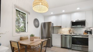 A modern kitchen with white cabinets, stainless steel appliances, and a wooden dining table. - New reno, Boho-style "treehouse" at the beach! (Kiawah Island)