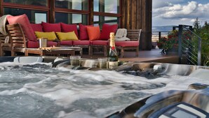 A hot tub with champagne, a wooden deck, a red sofa with cushions, and a mountain view.