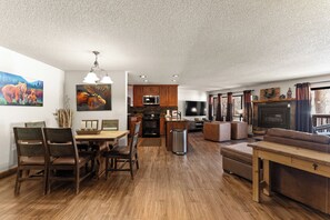 A spacious living area with a wooden floor, a dining table with chairs, a sofa, a fireplace, and a television.