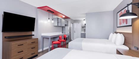 Een moderne hotelkamer met twee bedden, een televisie, een bureau met stoel en een kitchenette.