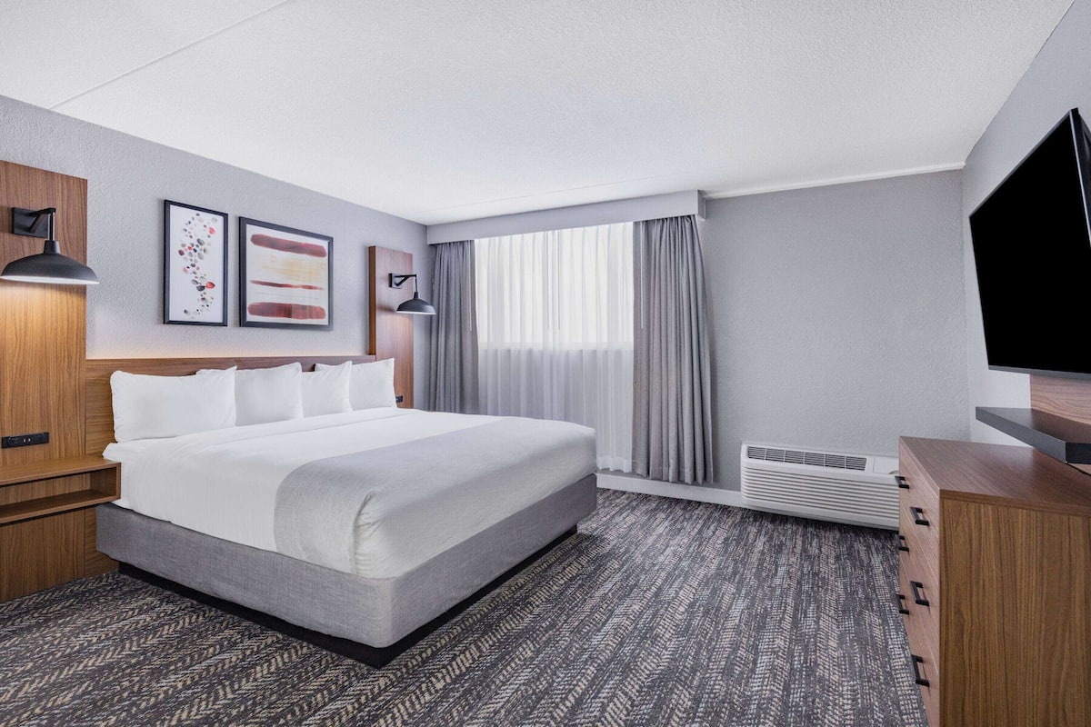 Una habitación de hotel con una cama grande, un escritorio con lámpara, televisión y ventana con cortinas.