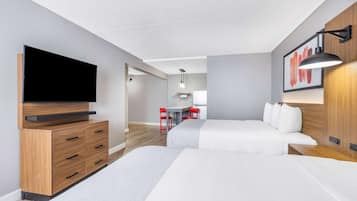 A modern hotel room with a flat-screen TV, wooden furniture, a desk with chairs, and a bed with white bedding.