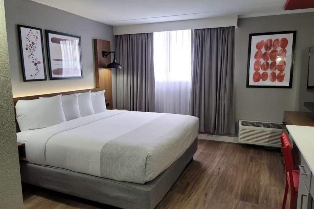 Habitación de hotel con una cama grande, un escritorio y una silla. Hay cortinas y una ventana.