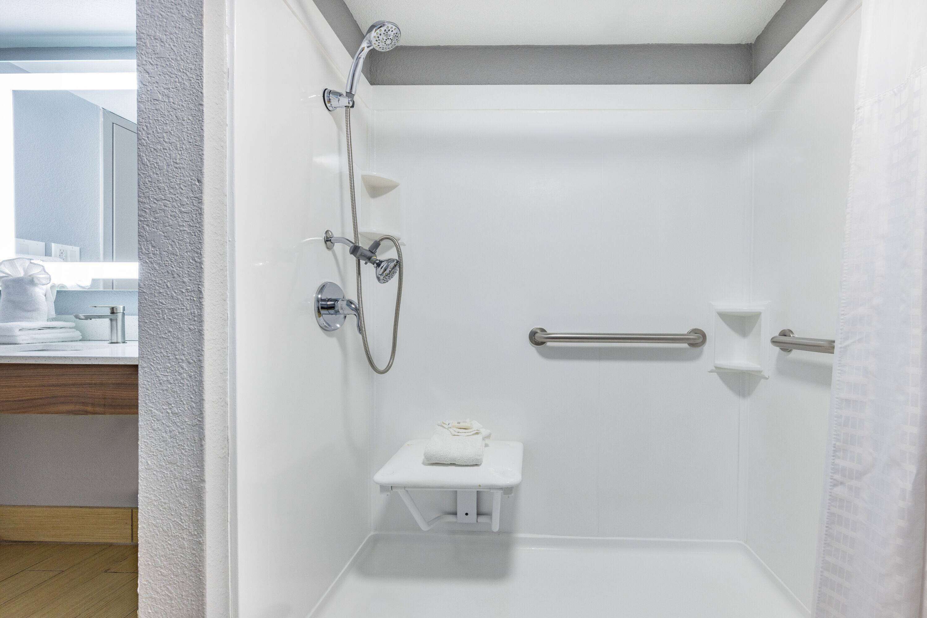 A small, white, walk-in shower with a handheld showerhead, a handheld showerhead, and a towel rack.