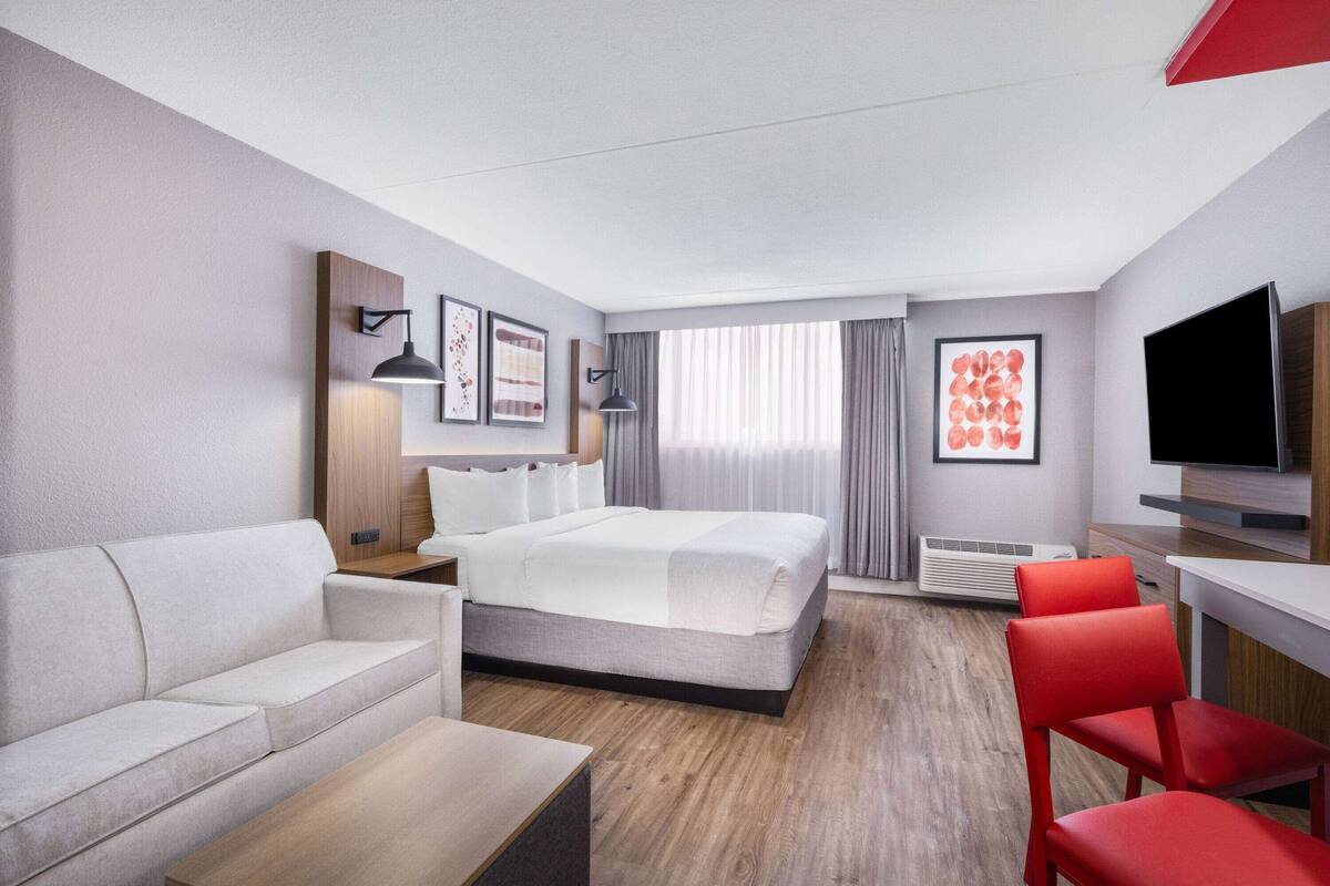 Una habitación de hotel moderna con cama, sofá, mesa de centro, televisor y escritorio.