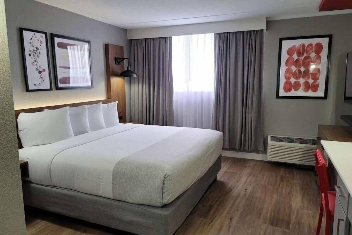 Una habitación de hotel con cama, escritorio, silla, lámpara y cortinas.