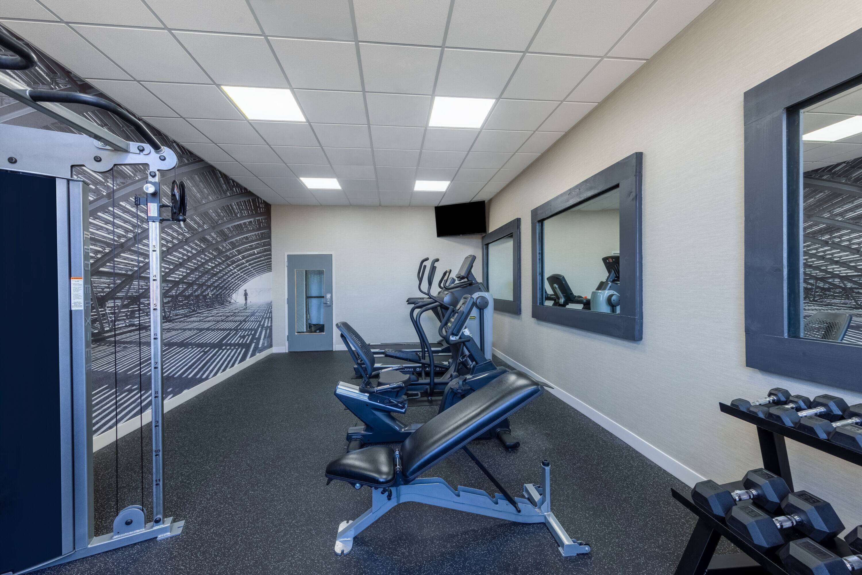 A gym with exercise equipment, a bench, and a mirror.
