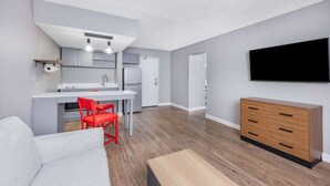 Een compacte leefruimte met kitchenette, een eethoek, een bank, een televisie en een houten kast.