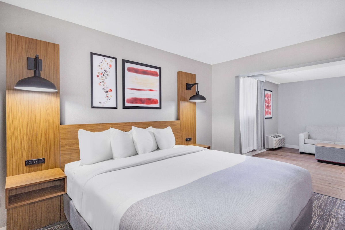 Una habitación de hotel moderna con una cama grande, cabecero de madera, dos lámparas fijadas a la pared y dos obras de arte enmarcadas.