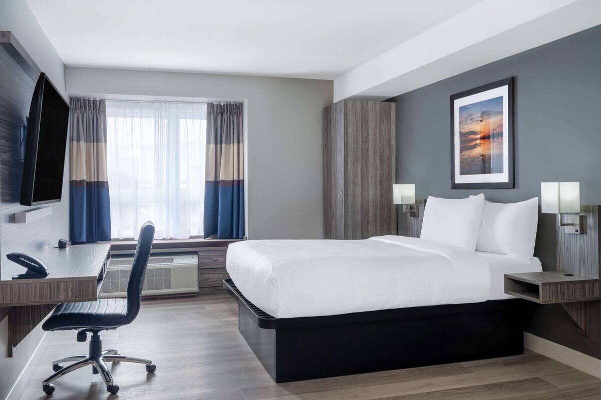 Une chambre d’hôtel avec un lit, un bureau, une chaise et une grande fenêtre avec des rideaux.