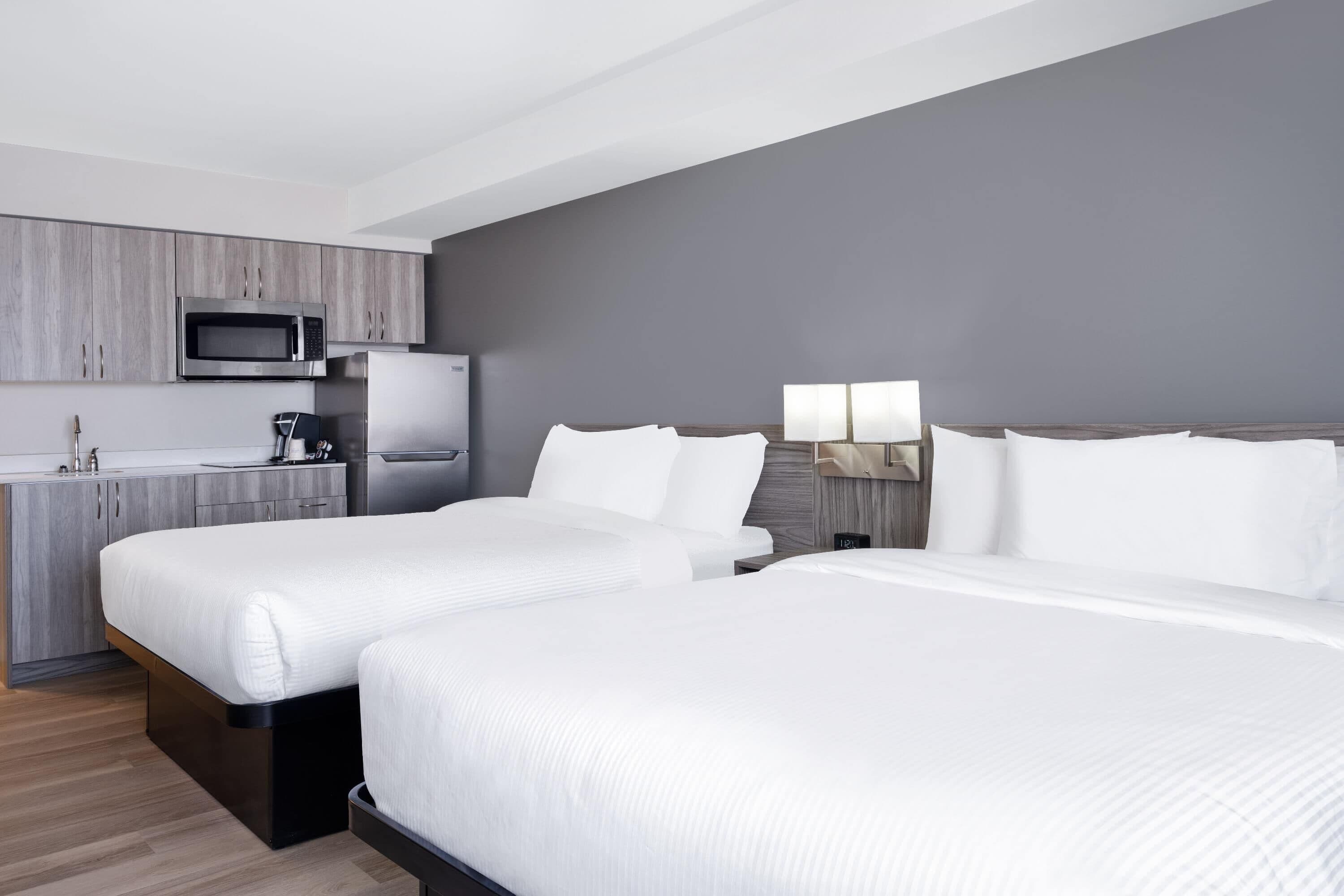 A hotel room with two beds, a kitchenette with a microwave, refrigerator, and coffee maker, and a bedside table with lamps.