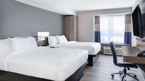 Habitación de hotel con dos camas, un escritorio, una silla y un televisor.
