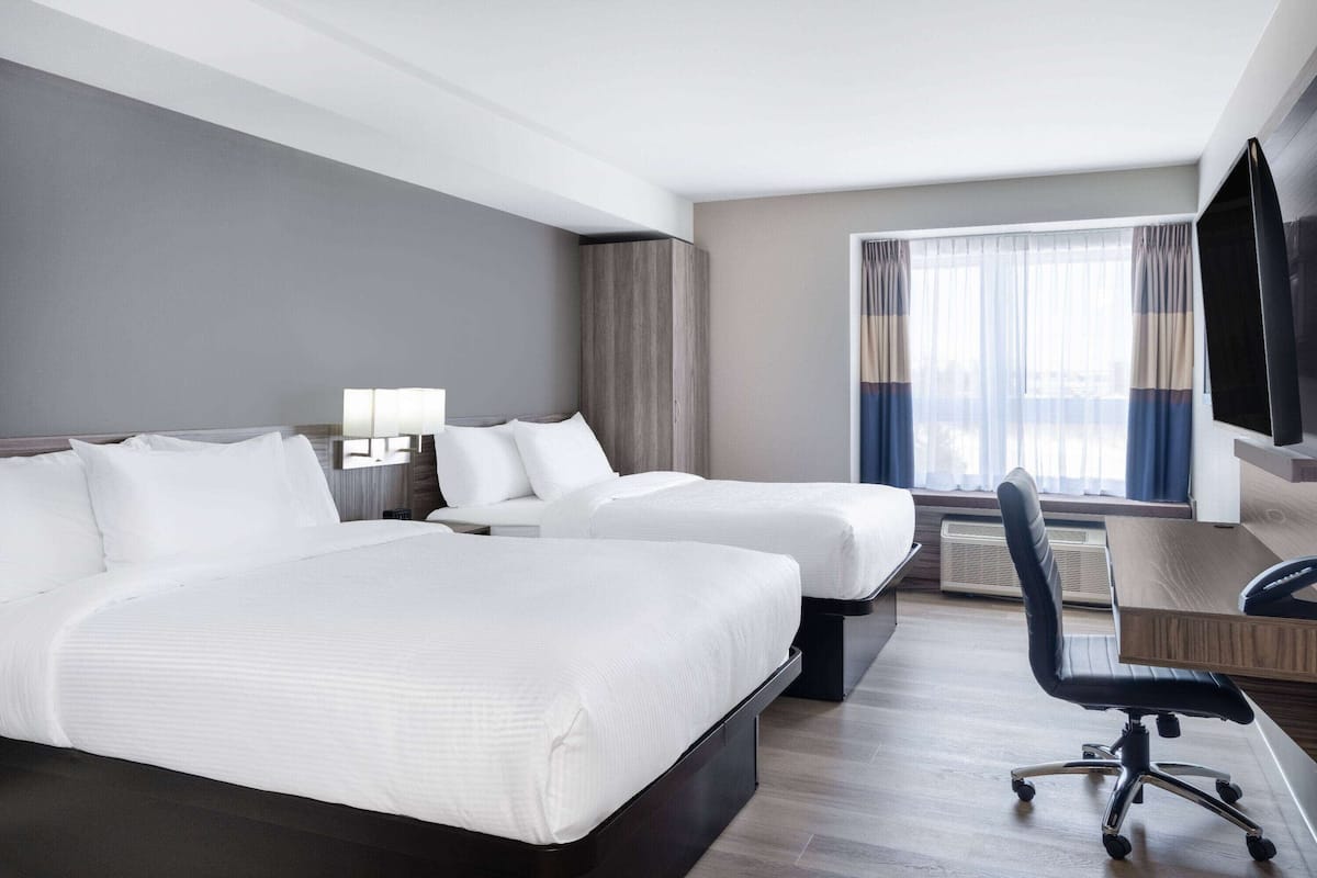 Une chambre d’hôtel avec deux lits, un bureau, une chaise et un téléviseur.