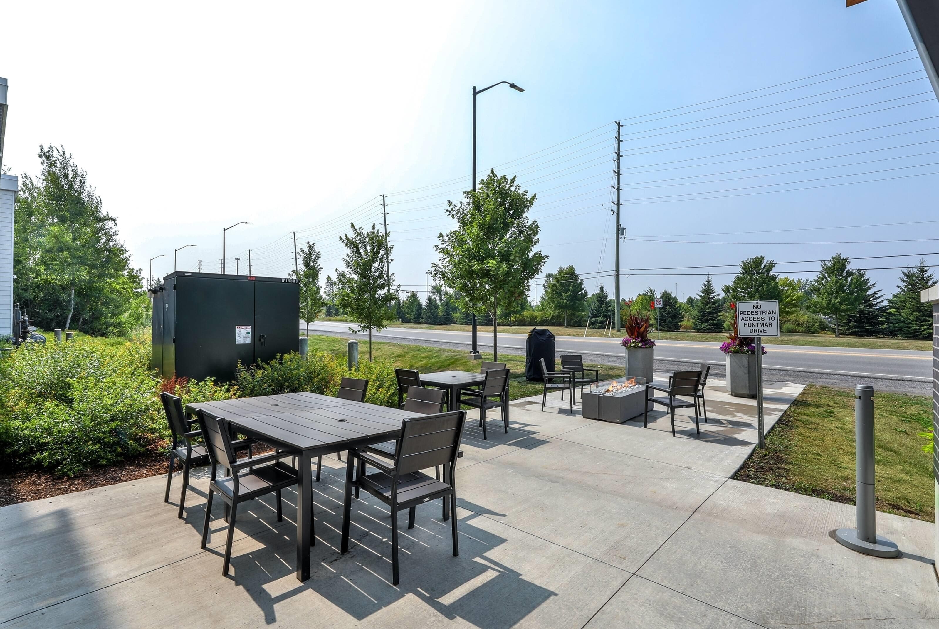 An outdoor seating area with tables and chairs, a fire pit, and a view of a road with a 'NO PEDESTRIAN ACCESS' sign.