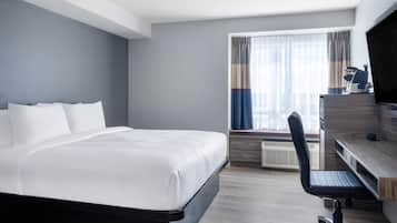 Habitación de hotel con una cama grande, un escritorio con silla y una ventana con cortinas.