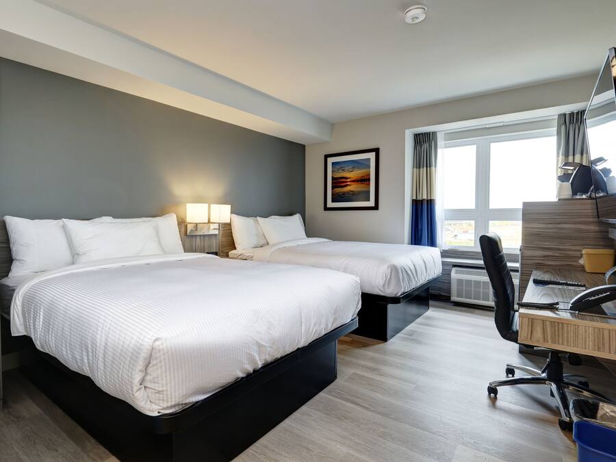 Habitación de hotel con dos camas, un escritorio con silla, una ventana con cortinas e imagen en la pared.