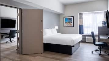Een moderne hotelkamer met een bed, bureau, stoel, televisie en een groot raam met gordijnen.