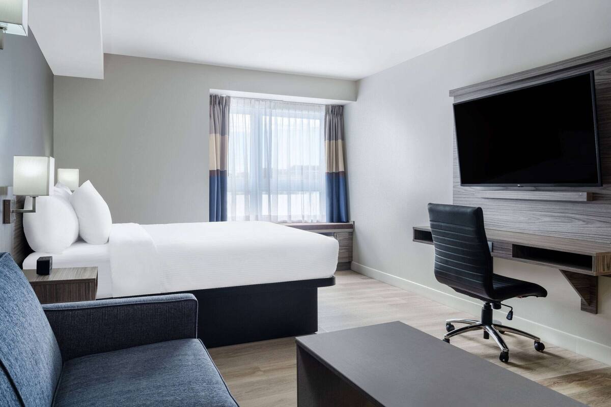 Une chambre d’hôtel avec un lit, un bureau, une chaise, une télévision et une fenêtre avec des rideaux.