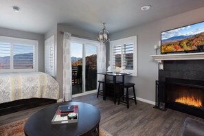 A modern living room with a fireplace, a television, a dining area, and a large window with a view of the mountains. - Incredible Mt. LeConte Views/Indoor Pool & Hot Tub (Gatlinburg)