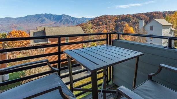 Un balcon avec une table et des chaises, donnant sur un paysage montagneux aux couleurs automnales.