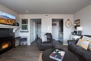 A living room with a fireplace, a television, a coffee table, and a leather armchair. - Incredible Mt. LeConte Views/Indoor Pool & Hot Tub (Gatlinburg)