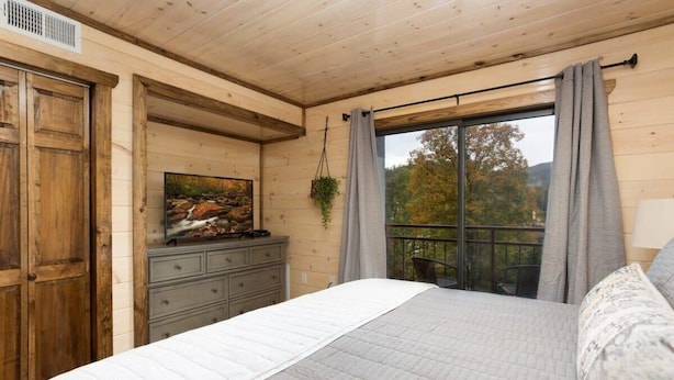 Un dormitorio con una cama grande, paredes de madera, un aparador, un cuadro y una ventana con cortinas.
