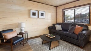 Una habitación acogedora con techo de madera, un sofá de cuero negro, una mesita de café negra y una mesita auxiliar con una lámpara.