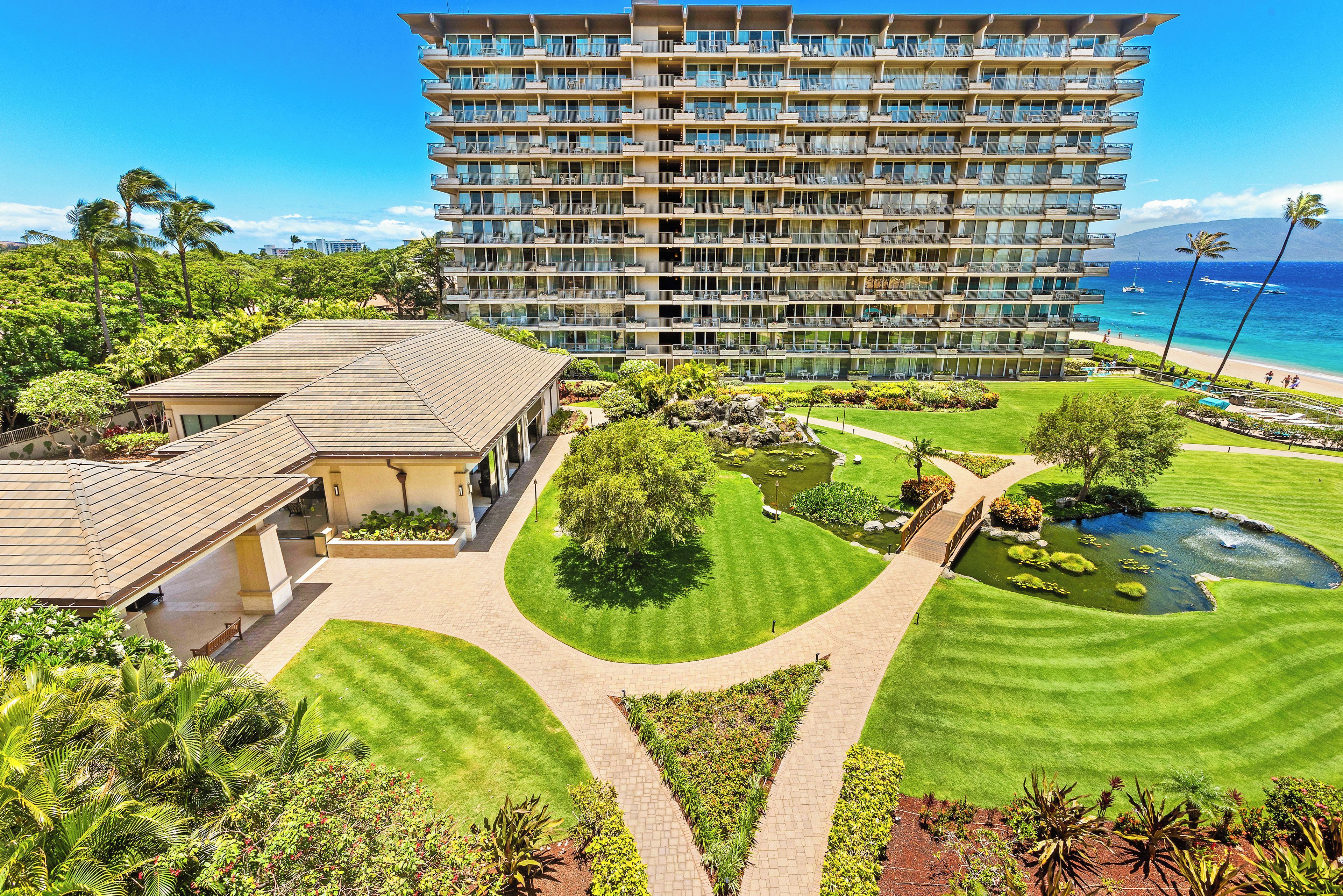 A high-rise hotel with a well-maintained garden, a pond, and a view of the beach and ocean.