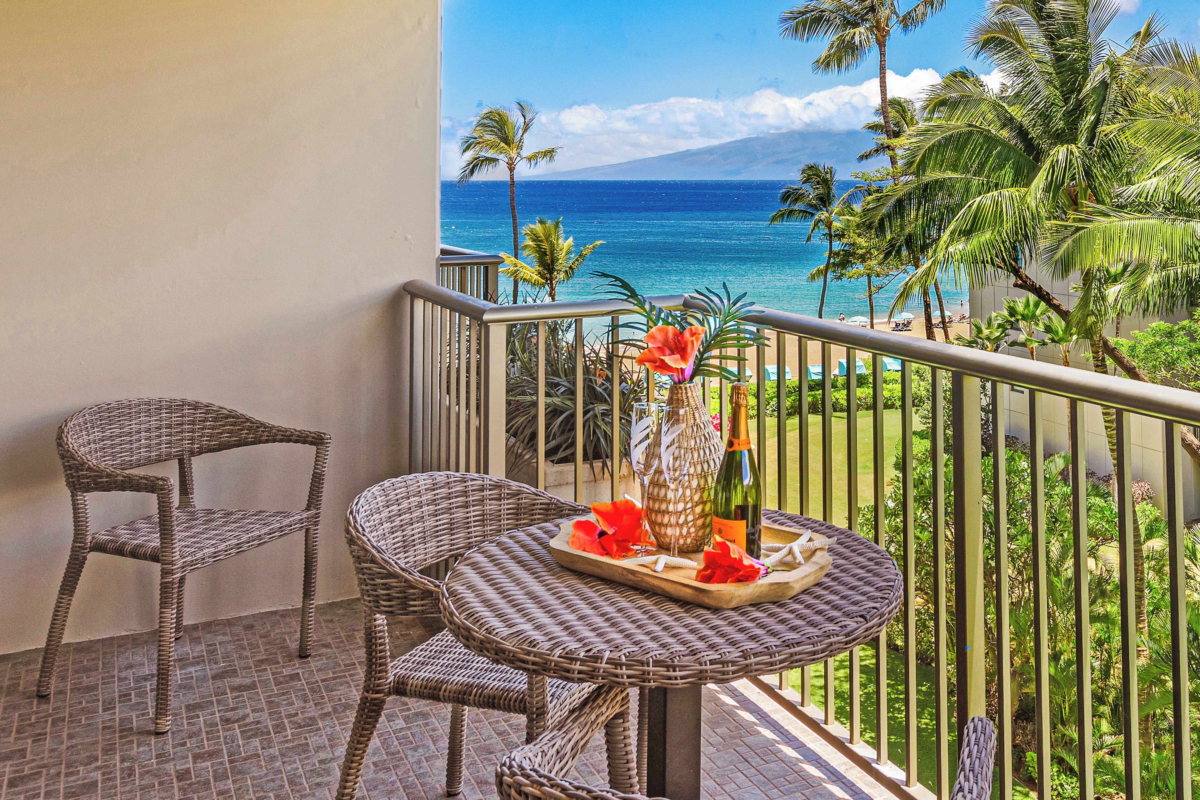 A balcony with wicker furniture, a vase with flowers, and a bottle.