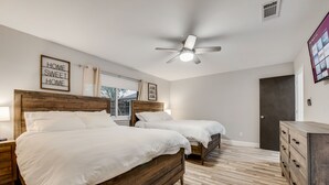 Une chambre avec deux lits, un ventilateur de plafond, un plancher en bois et une commode.