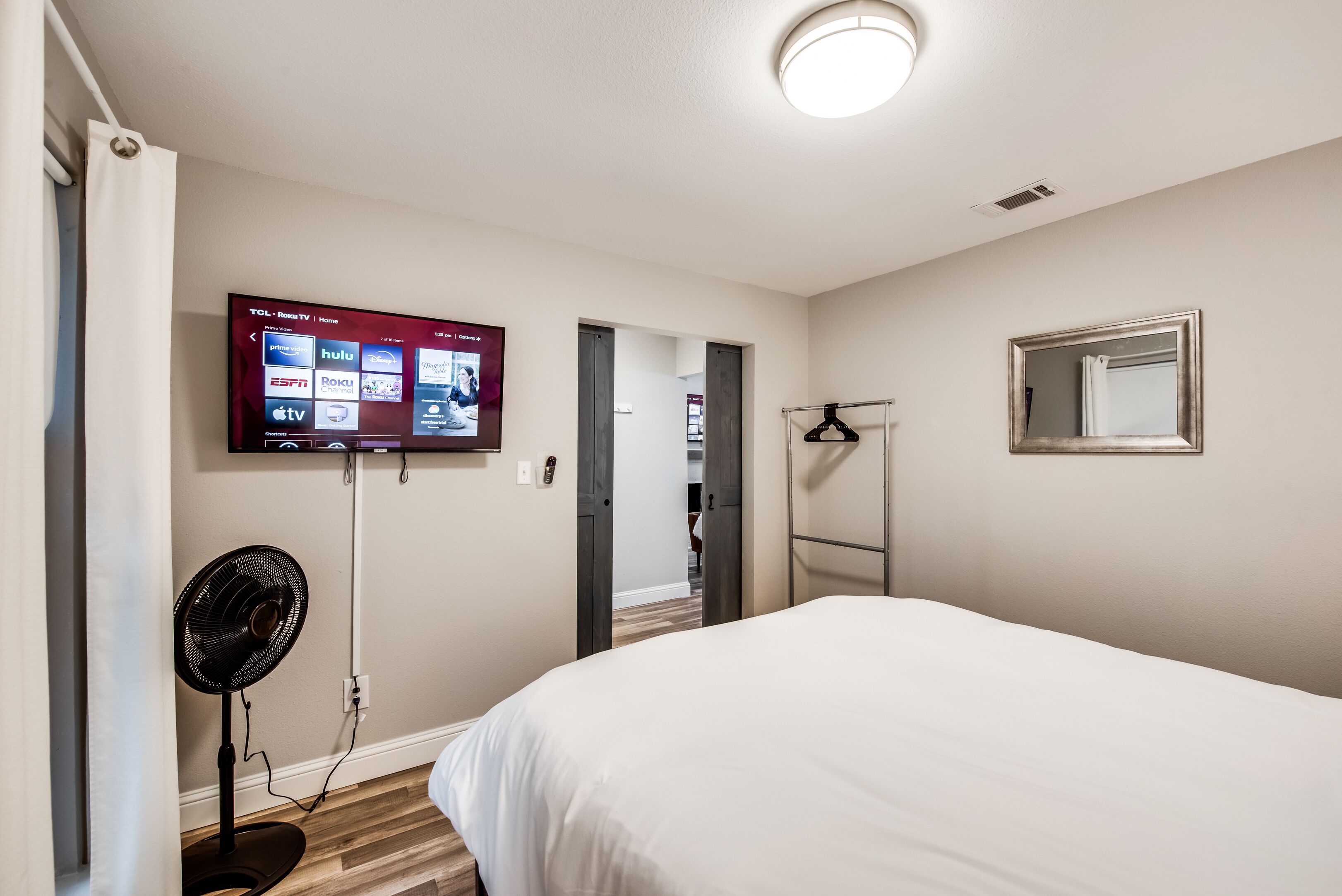 Habitación de hotel con cama, televisión montada en la pared mostrando diversas plataformas de streaming, ventilador y espejo.