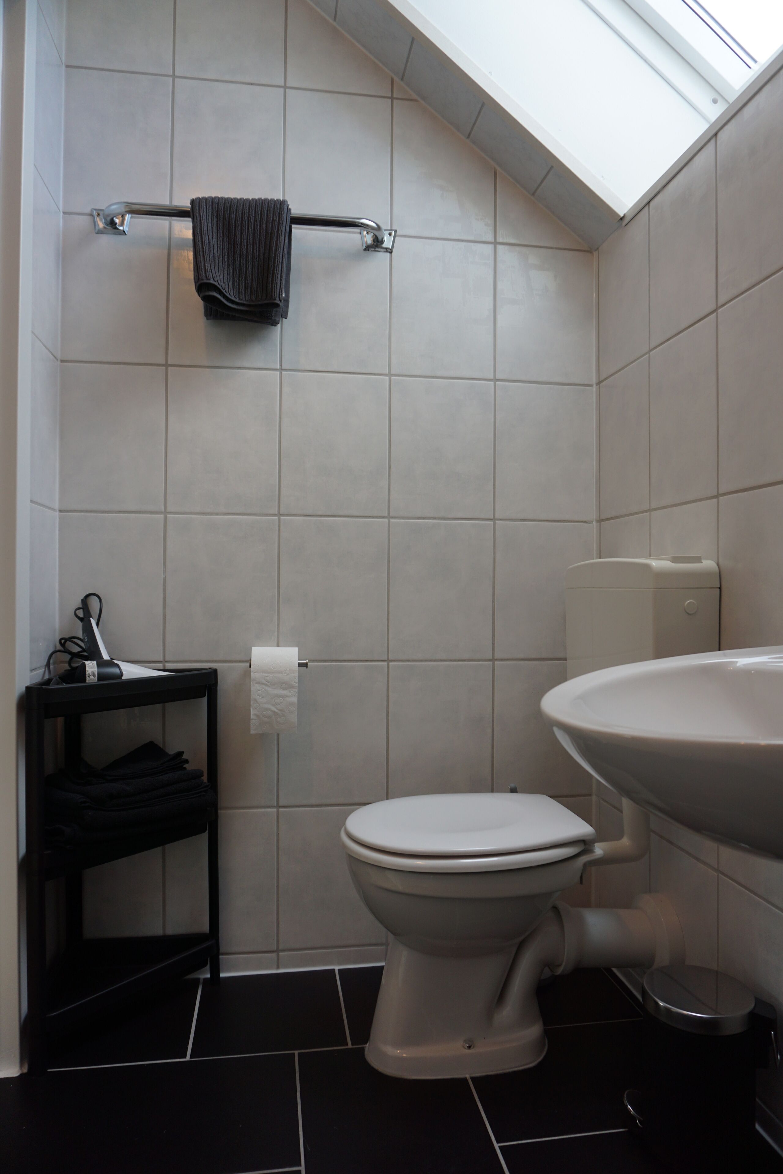 A compact bathroom with a toilet, a sink, a towel rack, and a shelf with folded towels.