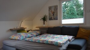 Un dormitorio con cama, ventana, planta y un cuadro.
