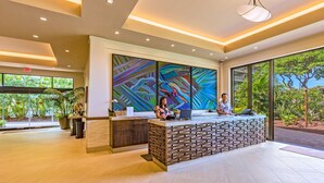 A reception area with a modern design, featuring a reception desk, large abstract artwork, and a view of greenery outside.