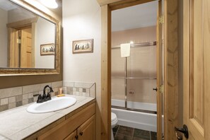 A bathroom with a sink, mirror, wooden vanity, and a shower area. - Beaver Creek West S2 2 Condo by RedAwning (Avon)