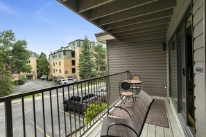 A balcony with a table and chairs, a view of a parking lot, and buildings in the background. - Beaver Creek West S2 2 Condo by RedAwning (Avon)
