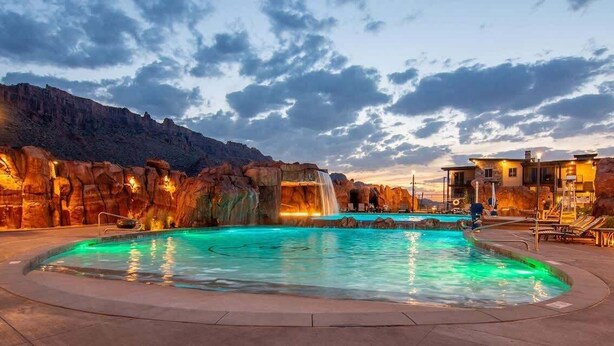 A pool with a waterfall feature, surrounded by rock formations and a mountain backdrop. - Sage Creek Resort E1 * Heated Pools * 2 Hot Tubs (Moab)