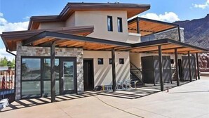 A modern two-story house with a stone facade, large glass windows, and a covered patio area. - Sage Creek Resort E1 * Heated Pools * 2 Hot Tubs (Moab)