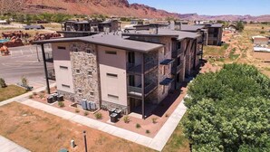 A modern multi-story building with a stone facade, balconies, and a parking lot. - Sage Creek E3 *Pet Ok* Pvt Hot Tub * Heated Pools (Moab)