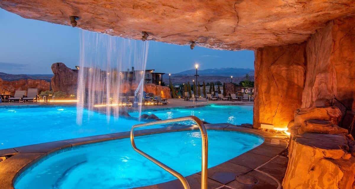 Une piscine agrémentée d’une cascade, entourée de formations rocheuses et de chaises longues.