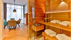 A modern hotel room with a wooden interior, a glass shower enclosure, a dining area with a table and chairs, and a visible clock on the wall. - Luxury Apartment "Strandperle" – First Row | Private Sauna | Family & Dog | Ocean View (Binz)