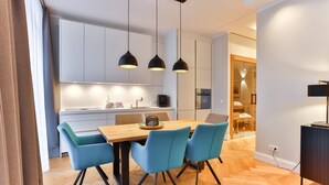 A modern kitchen with white cabinets, a wooden dining table, and blue chairs. There are pendant lights above the table and a small island with a coffee machine. - Luxury Apartment "Strandperle" – First Row | Private Sauna | Family & Dog | Ocean View (Binz)