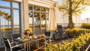 Eine sonnendurchflutete Terrasse mit einem Frühstückstisch, mit Blick auf einen Strand.