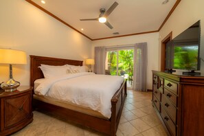 Camera d'albergo con un letto, lampade da comodino, una ventola a soffitto, una televisione e vista su del verde dalla finestra.