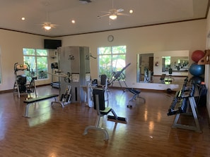 Een sportschool met trainingsapparatuur, grote ramen en een spiegel.