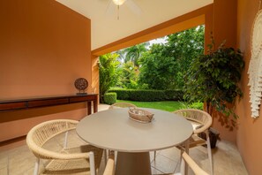 A patio with a round table and four wicker chairs, surrounded by orange walls and a view of a lush garden.